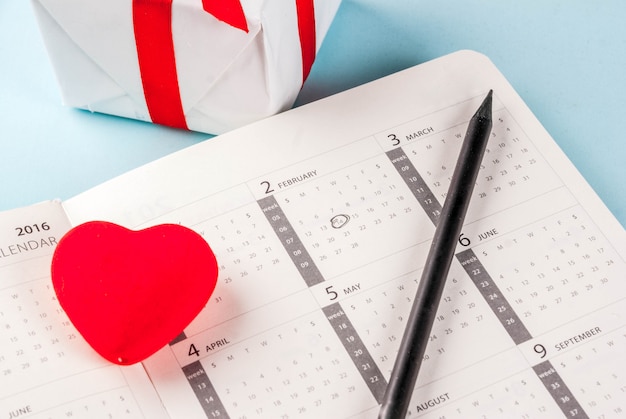 Tarjeta de felicitación del día de San Valentín. Corazón rojo con caja de regalo sobre el calendario de febrero sobre fondo azul claro. Copiar espacio para saludos