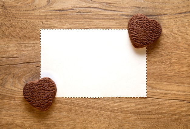 Tarjeta de felicitación del día de San Valentín con dos galletas de chocolate en forma de corazón al horno sobre fondo de madera. Vista superior, espacio vacío para texto. Endecha plana