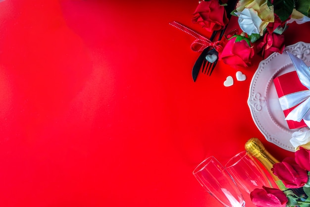 Tarjeta de felicitación del día de San Valentín con ramo de flores rosas rojas, vino y caja de regalo en la mesa roja. Vista superior con espacio para saludos. Fondo del día de san valentín plano laico