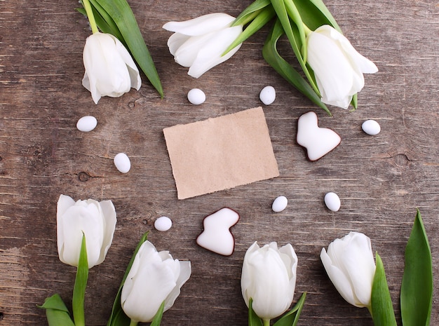 Tarjeta de felicitación feliz de Pascua con los huevos blancos del tulipán y de chocolate y el conejito, fondo rústico.