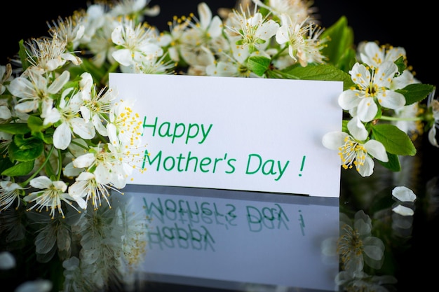 Tarjeta de felicitación para la madre y la floreciente rama primaveral con flores aisladas en el fondo negro