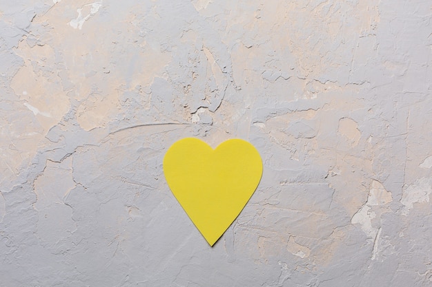 Tarjeta de felicitación minimalista del día de San Valentín en Pantone 2021 colores gris y amarillo, corazón de papel sobre fondo texturizado, endecha plana