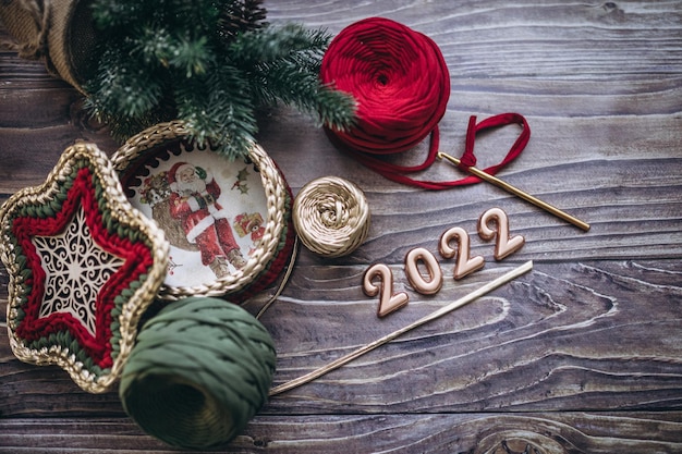 Tarjeta de felicitación de Navidad y año nuevo 2022, bolas de hilo de punto, ganchillo y canasta tejida sobre una mesa de madera, vista superior