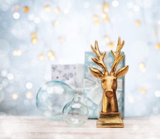 Tarjeta de felicitación de Navidad o año nuevo con ciervos dorados, cajas de regalo y adornos navideños en la mesa. Bodegón festivo con bokeh.