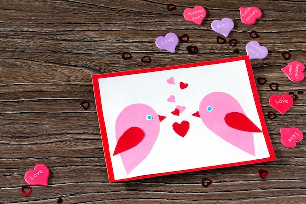 Tarjeta de felicitación para niños Dos pájaros y corazón de un papel en el día de San Valentín.