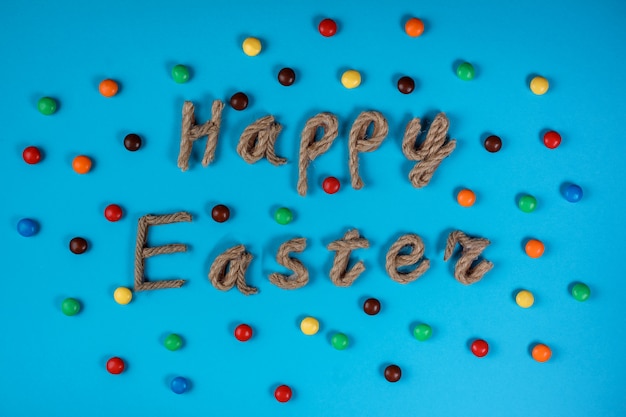 Tarjeta de felicitación o invitación de Pascua feliz, tipografía de cuerda y dulces de gragea sobre fondo azul. Tarjeta de felicitación de Pascua: tipografía de cuerda Feliz Pascua entre dulces grageas de colores sobre fondo azul.