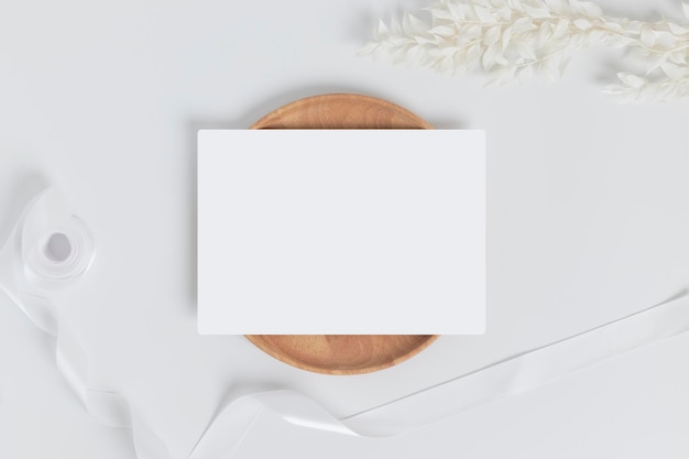 Tarjeta de felicitación o tarjeta de invitación con hojas de flores secas blancas en placa de madera o bandeja en la vista superior de fondo blanco