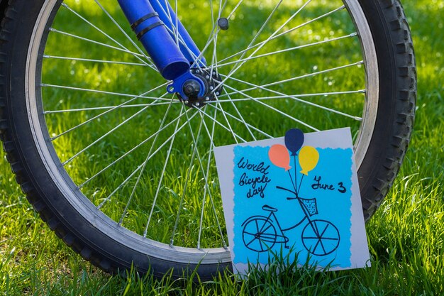 Tarjeta de felicitación de papel de colores hechos a mano junto a una rueda de bicicleta sobre fondo de hierba. Bricolaje. Día mundial de la bicicleta.