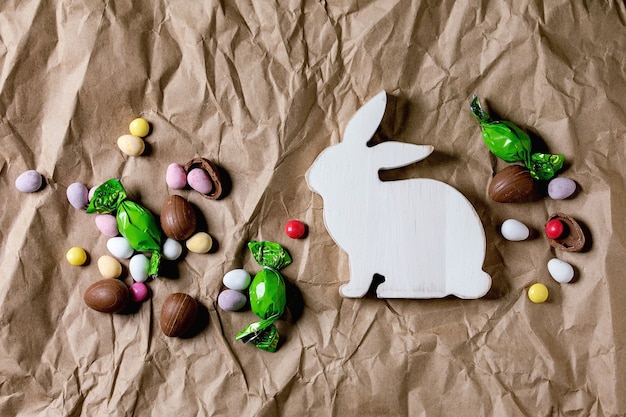 Tarjeta de felicitación de Pascua con adornos de conejo de madera, dulces de chocolate y huevos en papel artesanal arrugado