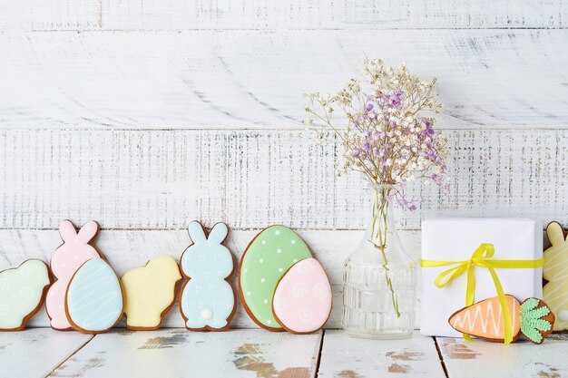 Tarjeta de felicitación de Pascua con coloridos conejos, huevos, gallinas y zanahorias galletas de jengibre sobre fondo blanco de madera vieja con espacio de copia. Vista superior.