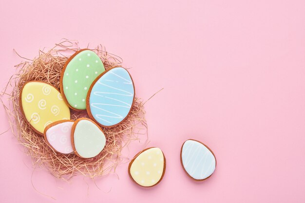 Foto tarjeta de felicitación de pascua con coloridos conejos, huevos, gallinas y zanahorias, galletas de jengibre sobre fondo rosa con espacio de copia. vista superior.