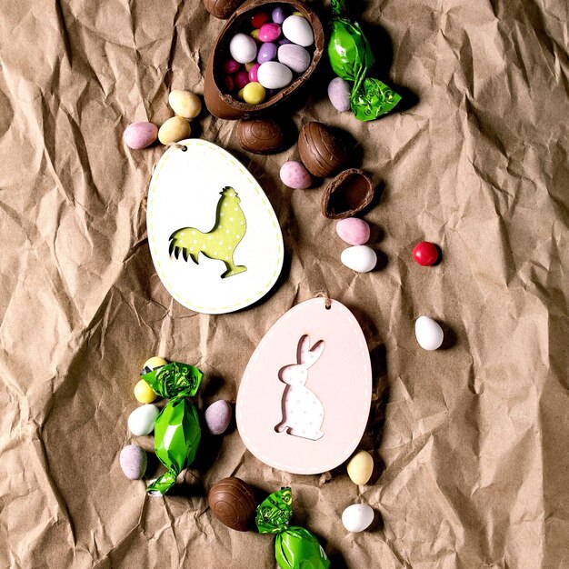 Tarjeta de felicitación de Pascua con decoraciones de conejo y pollo de madera, dulces de chocolate y huevos sobre fondo de papel artesanal arrugado. Endecha plana, copie el espacio. imagen cuadrada