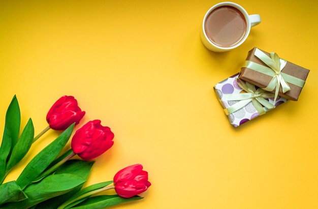 Tarjeta de felicitación plana pone una taza de café caliente y un ramo de tulipanes rojos sobre fondo amarillo brillante