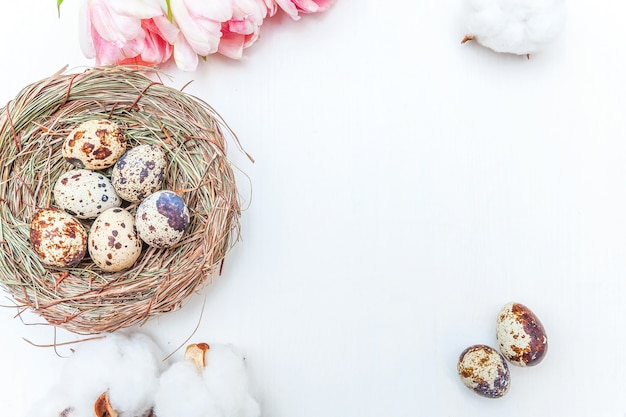 Tarjeta de felicitación de primavera. Huevos de Pascua en nido de algodón y ramo de flores de tulipán fresco rosa sobre fondo de madera blanca rústica