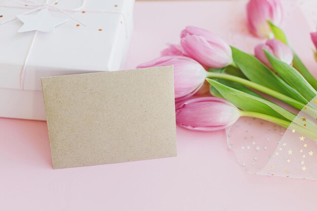 Tarjeta de felicitación vacía ramo de tulipanes rosas y caja de regalo sobre fondo rosa Plantilla de tarjeta de felicitación