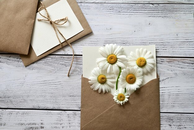 Una tarjeta de felicitación vacía con un sobre marrón y una flor blanca para mamá en una mesa de madera de estilo antiguo y con viñetas