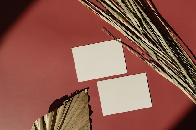 Tarjeta de hoja de papel en blanco con espacio de copia de maqueta sobre fondo rojo con silueta de sombras de luz solar Hoja de palma tropical seca Plantilla de marca comercial mínima bohemia estética Vista plana superior