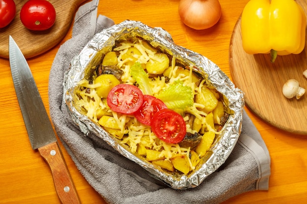 Foto una tarjeta horneada con queso decorada con tomates en una lámina en forma de toalla sobre una mesa de madera junto a verduras, cebollas, tomates y un cuchillo