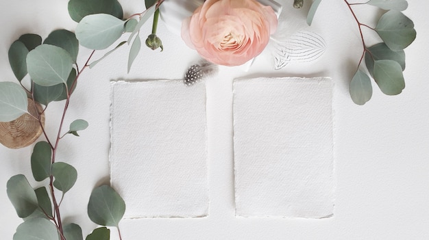Tarjeta de invitación de saludo de boda blanca en blanco rama de hojas de eucalipto de plata, flor de ranúnculo de ranúnculo rosa rubor sobre fondo de mesa de papel con textura. Plantilla moderna elegante vista superior plana