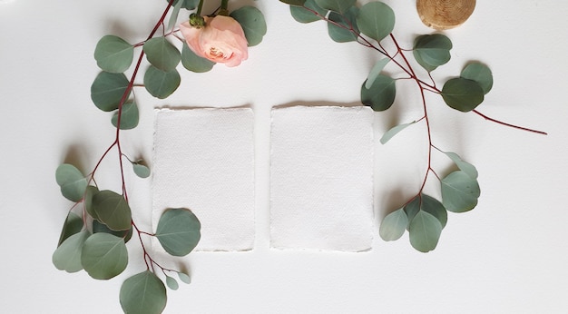 Foto tarjeta de invitación de saludo de boda blanca en blanco rama de hojas de eucalipto de plata, flor de ranúnculo de ranúnculo rosa rubor sobre fondo de mesa de papel con textura. plantilla moderna elegante vista superior plana