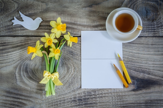 Tarjeta de invitación vacía con narcisos y una taza de té sobre fondo de madera