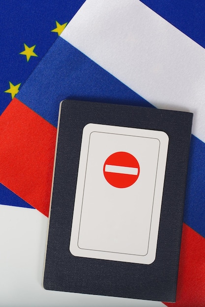 Tarjeta con un letrero de acceso prohibido colocado en un pasaporte de servicio de un funcionario internacional. Dos banderas de la UE y Rusia en el fondo. Vista superior. Espacio libre para un texto