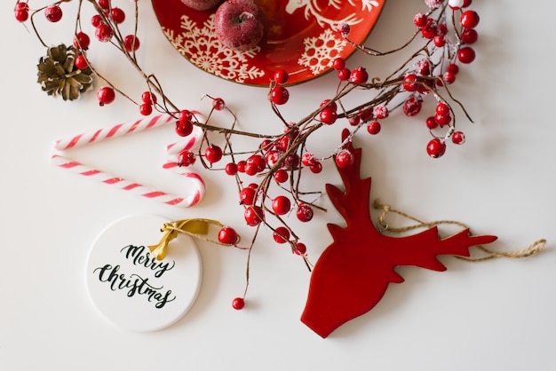 Tarjeta de Navidad y año nuevo en rojo y blanco. Decoraciones navideñas, bayas rojas y dulces