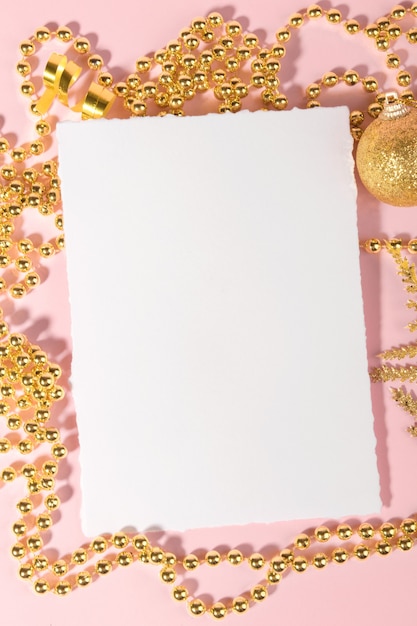 Foto tarjeta de navidad con decoración festiva dorada sobre un fondo rosa pastel.