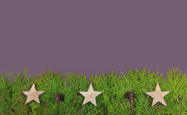 Tarjeta de Navidad plana sobre fondo violeta con ramas y conos de Thuja y estrellas de madera.