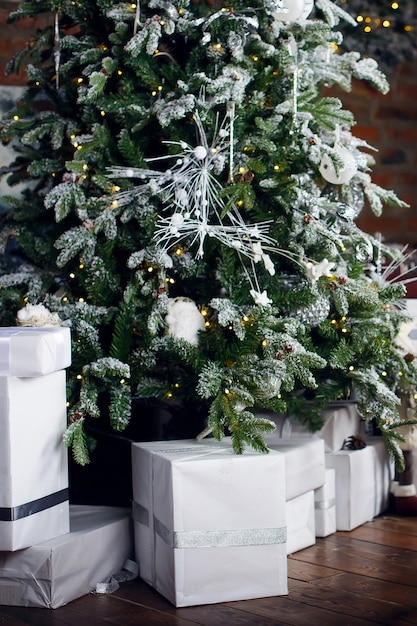 Tarjeta de Navidad. Los regalos en cajas de embalaje blanco liso se encuentran debajo de un árbol de Navidad sobre un piso de madera marrón.