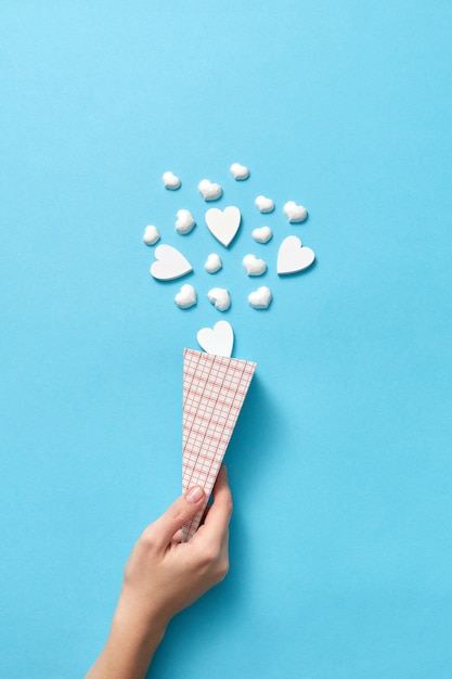 Tarjeta navideña creativa con cono de papel de pequeños corazones de yeso como postre helado en la mano de una mujer