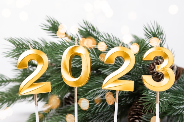 Tarjeta navideña con números 2023 en color dorado y luces desenfocadas ramas de abeto verde