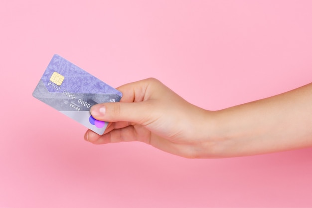 Tarjeta de pago de plástico en una mano femenina, sobre un rosa claro
