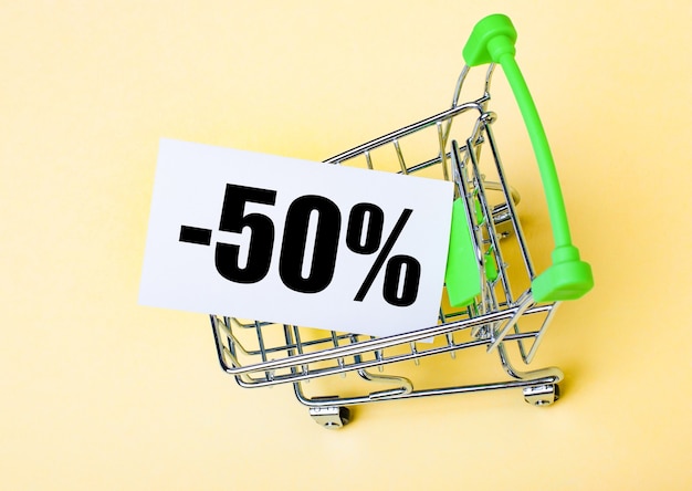 La tarjeta con las palabras MENOS CINCUENTA POR CIENTO está en el carrito de compras. Concepto de marketing.