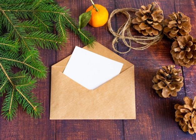 Tarjeta de papel blanco en blanco en un sobre marrón hecho a mano sobre una vieja mesa de madera en un estilo navideño Ramas de abeto mandarina y conos están sobre la mesa Navidad y Año Nuevo