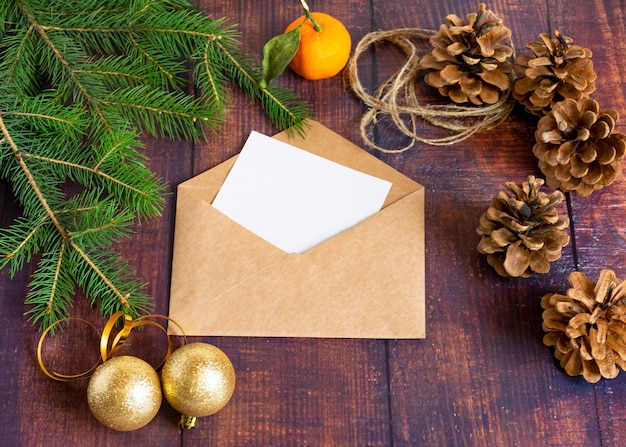 Tarjeta de papel blanco en blanco en un sobre marrón hecho a mano sobre una vieja mesa de madera en un estilo navideño Ramas de abeto mandarina y conos están sobre la mesa Navidad y Año Nuevo