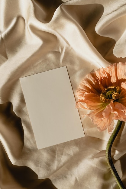 Tarjeta de papel en blanco con copia de maqueta espacio flor de amapola con sombras estéticas de luz solar en tela dorada arrugada plantilla de invitación de boda estética vista superior plana