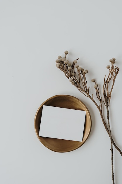 Tarjeta de papel en blanco con espacio de copia en placa de latón rama floral seca sobre fondo blanco Vista superior plana concepto de marca de negocio bohemio de lujo estético minimalista