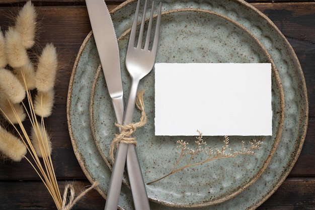 Foto tarjeta de papel en blanco en un plato con tenedor y cuchillo en la mesa con decoración bohemia y plantas secas