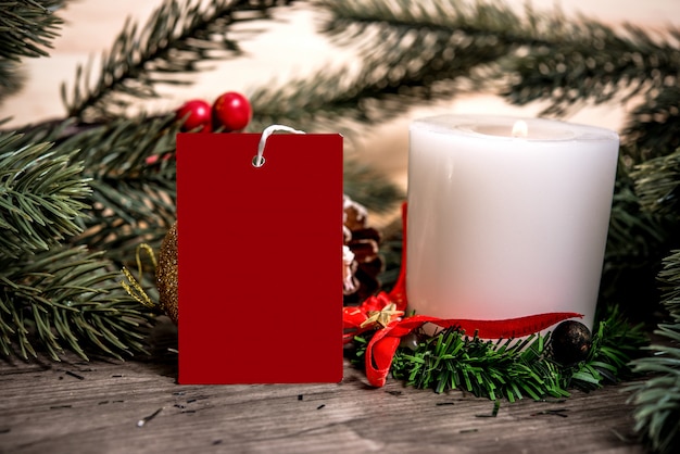 Tarjeta de papel de la etiqueta de la maqueta con la decoración de la Navidad de la vela en el fondo de madera de la tabla.