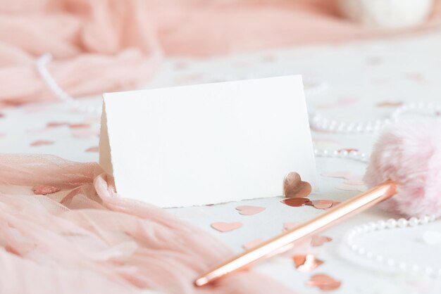 Foto tarjeta plegada cerca de decoraciones rosadas corazones y tulle en mesa blanca maqueta de primer plano