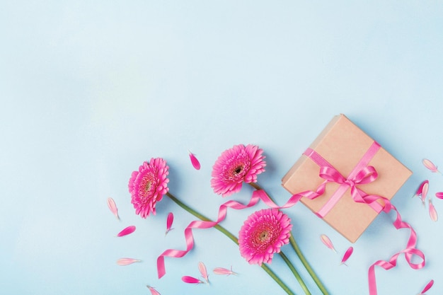 Tarjeta de primavera para el cumpleaños de la mujer o el día de la madre Flores rosadas y caja de regalos en la mesa azul vista superior Fl