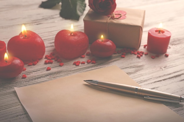 Tarjeta de regalo para el Día de San Valentín con caja de bolígrafos y velas sobre fondo blanco de madera