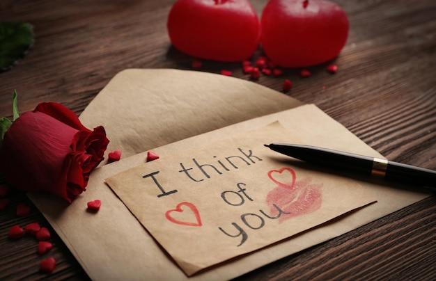 Tarjeta de regalo para el Día de San Valentín con pluma de rosa roja de inscripción y velas sobre fondo de madera