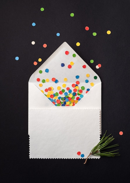 Tarjeta de regalo de Navidad en sobre blanco con confeti festivo. Hoja de papel de nota sobre fondo negro