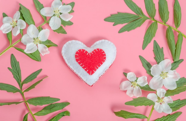 Tarjeta de San Valentín, corazón rojo con un marco de flores y hojas sobre un fondo rosa