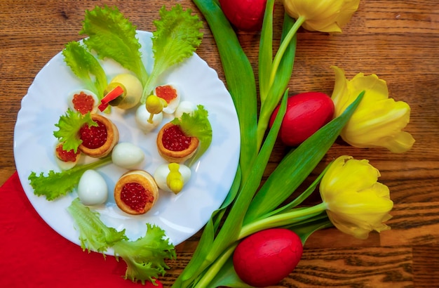 Tarjeta de vacaciones de Pascua con huevos rojos y flores de tulipán amarillo en la mesa de madera