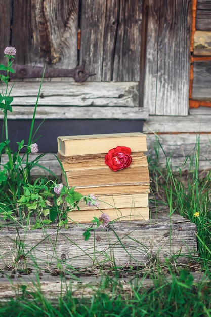 Tarjeta vintage con pila de libros antiguos y flor de rosa al aire libre