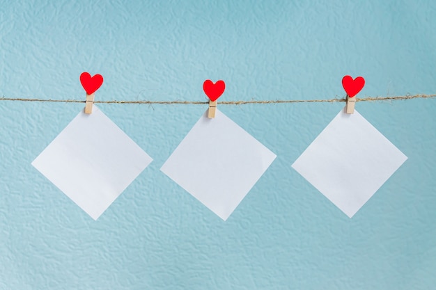 Tarjetas en blanco en alfileres con corazones rojos. Maqueta para texto y fondo azul para saludos del día de San Valentín