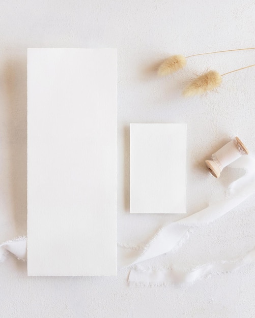 Tarjetas en blanco cerca de cintas de seda y vista superior de hierba de cola de liebre seca en maqueta boho blanca